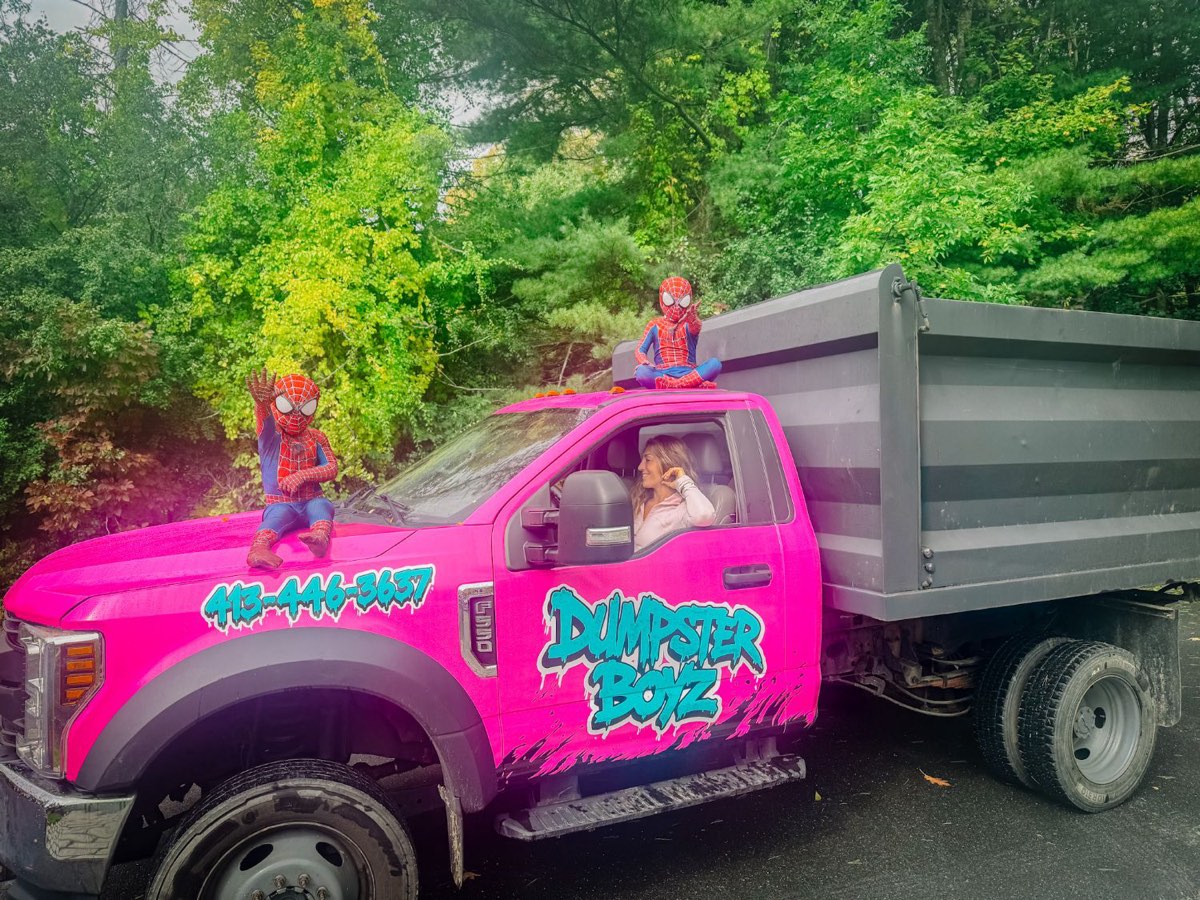 Gabrielle at the wheel of the hot-pink Dumpster Boyz truck, with her two boys in superhero costumes on the hood and the roof.